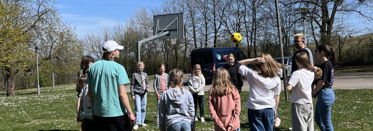 Gruppe steht im Kreis und wirft einen Ball